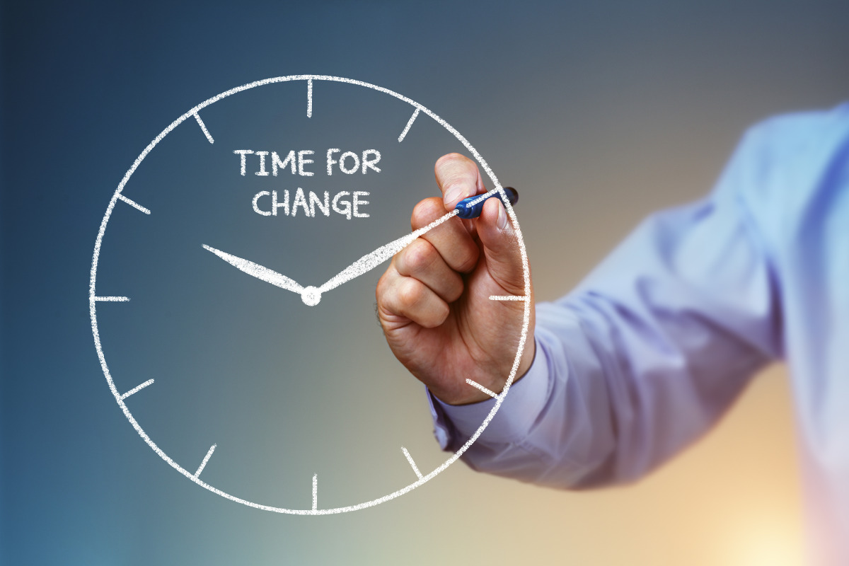 Businessman's hand drawing a clock on a whiteboard with text 'Time For Change'