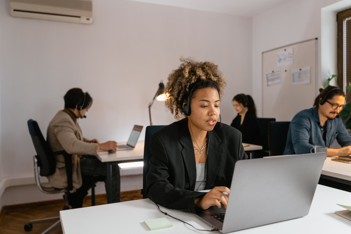 A team of coworkers at the office working on laptops while wearing headsets catering to their clients via VoIP solutions with features such as call forwarding