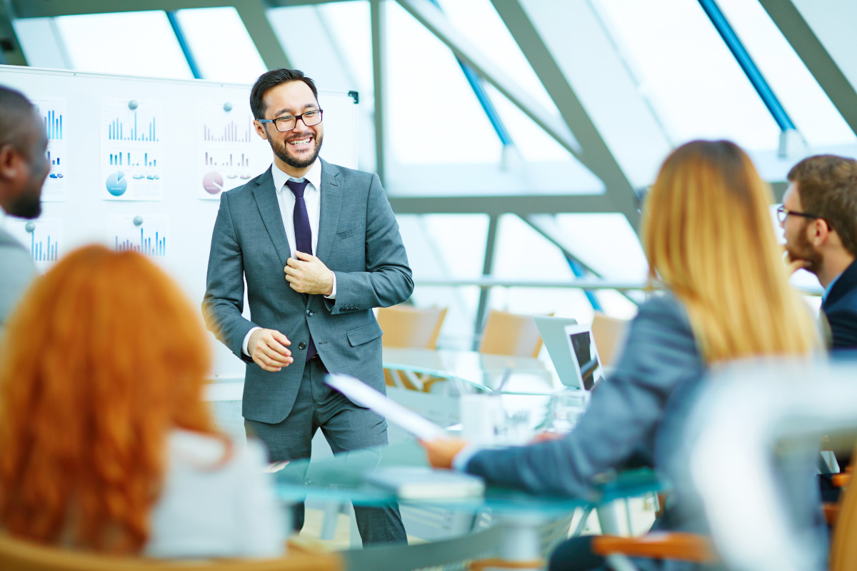 A man in a suit smiling while presenting data to people in business attire