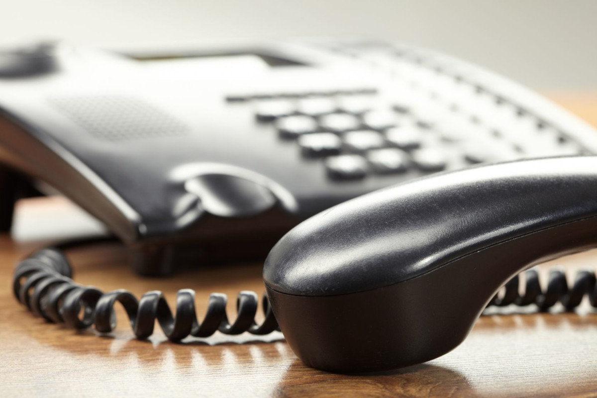 A phone on a desk, with the receiver placed down in the foreground.