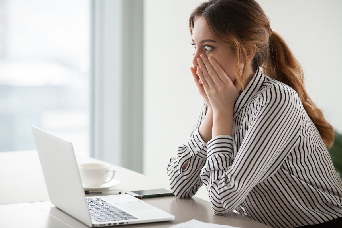 Shocked woman looking at laptop screen surprised with hands over mouth. Mistake or bad news concept.