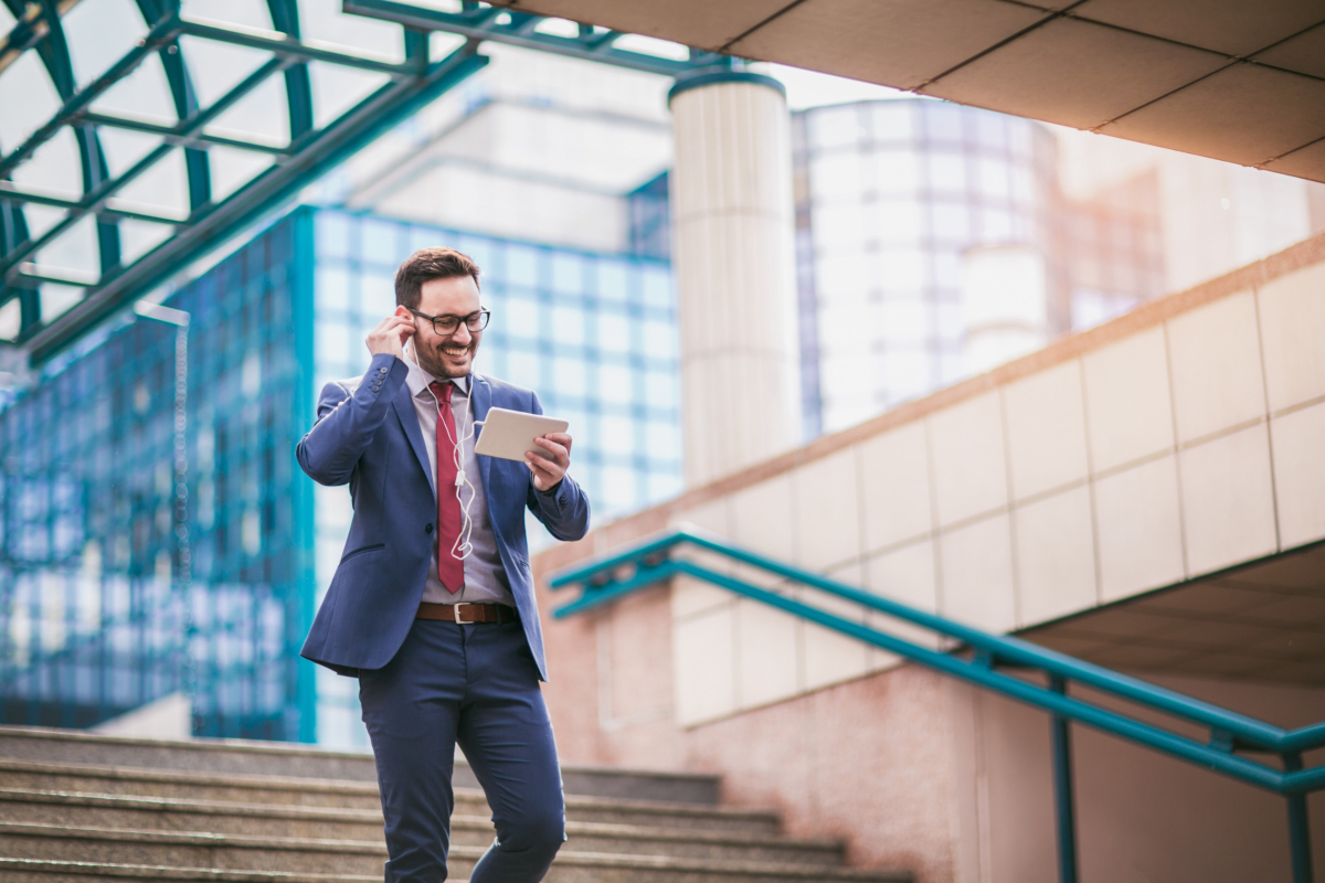 Man walking in front of building laughing and using tablet