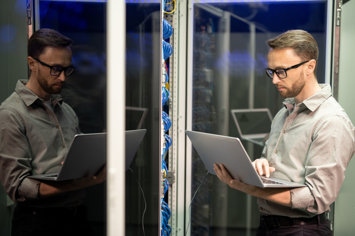 A person holding a laptop analysing network hardware