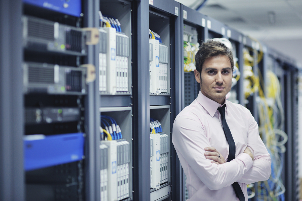 A person in a button up shirt and tie standing in front of network hardware