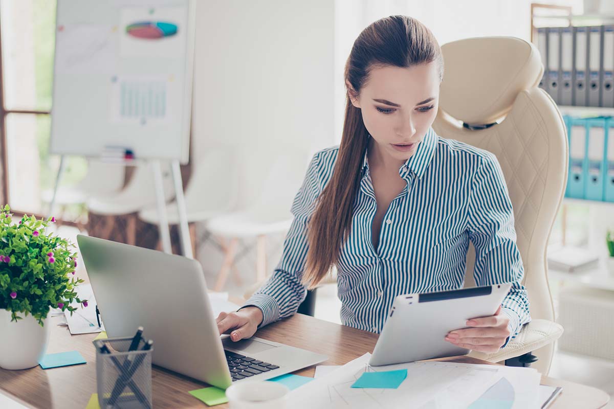 Young business woman using mobile devices while seated at desk in home or casual modern office.