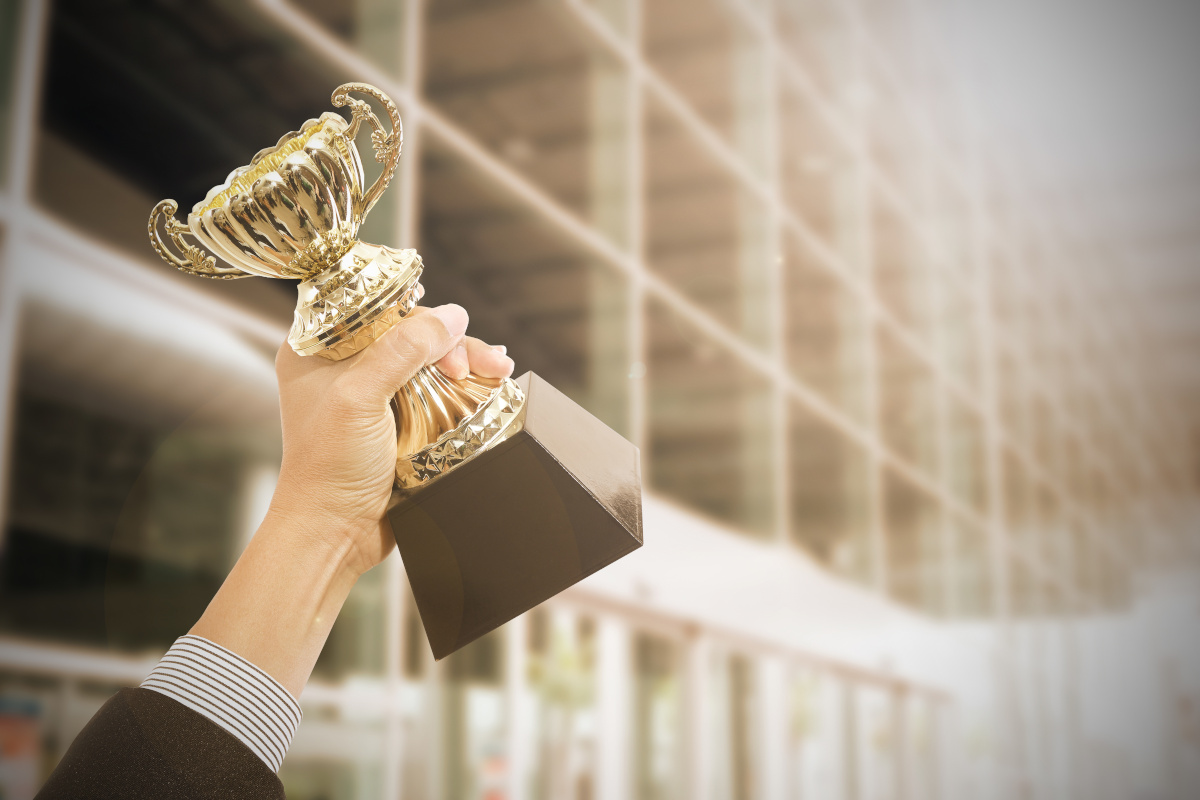 Close up of business person's hand holding up a gold trophy.