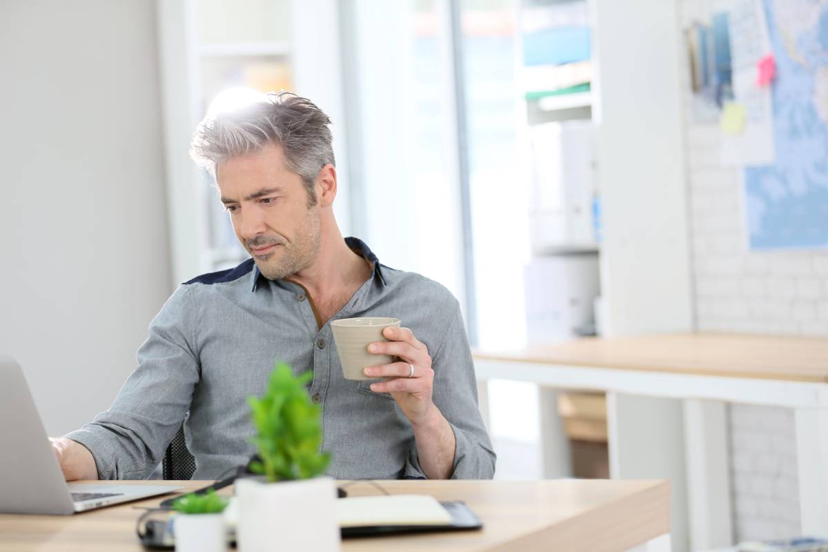 A man working from using a laptop and drinking coffee