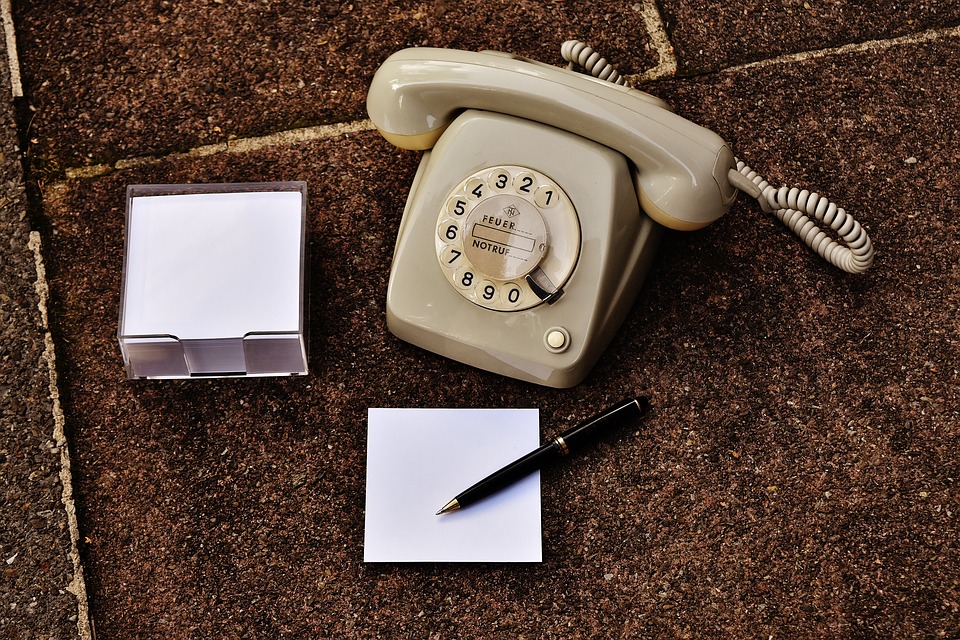 Old style rotary phone next to a pen and a pad of paper