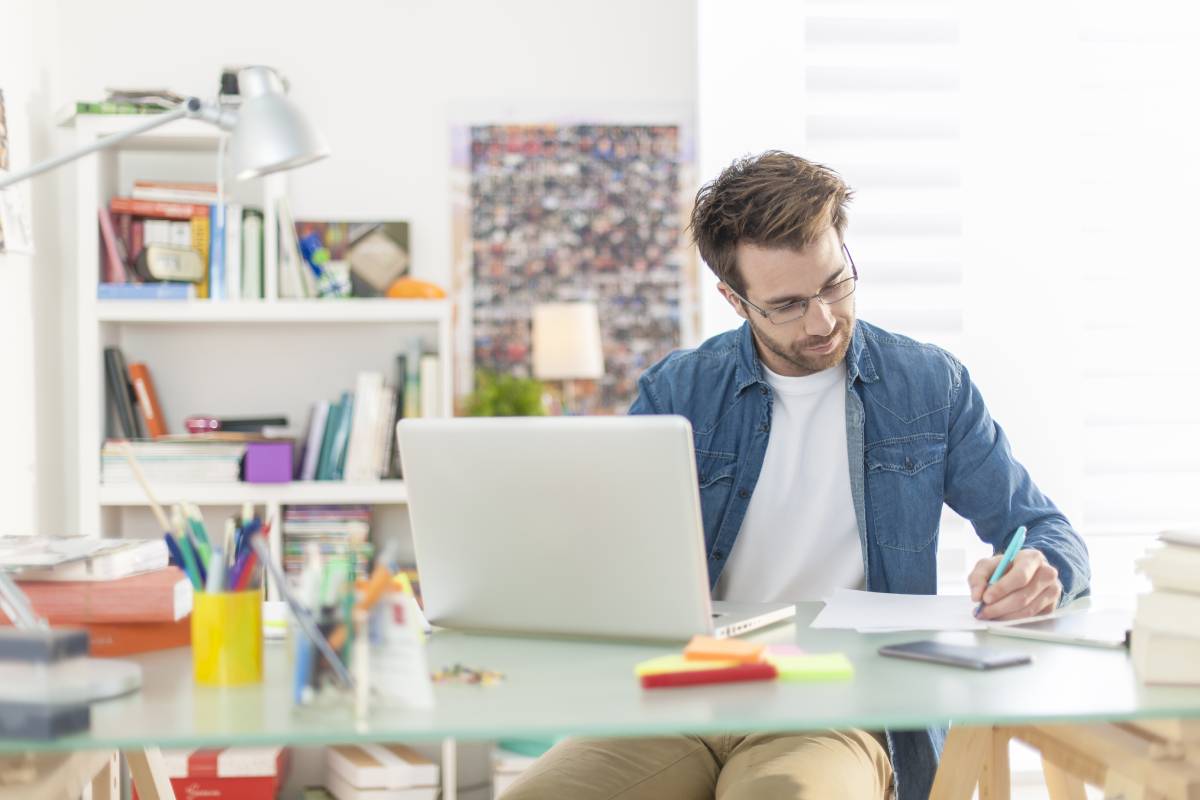 A man working from home using a computer and writing