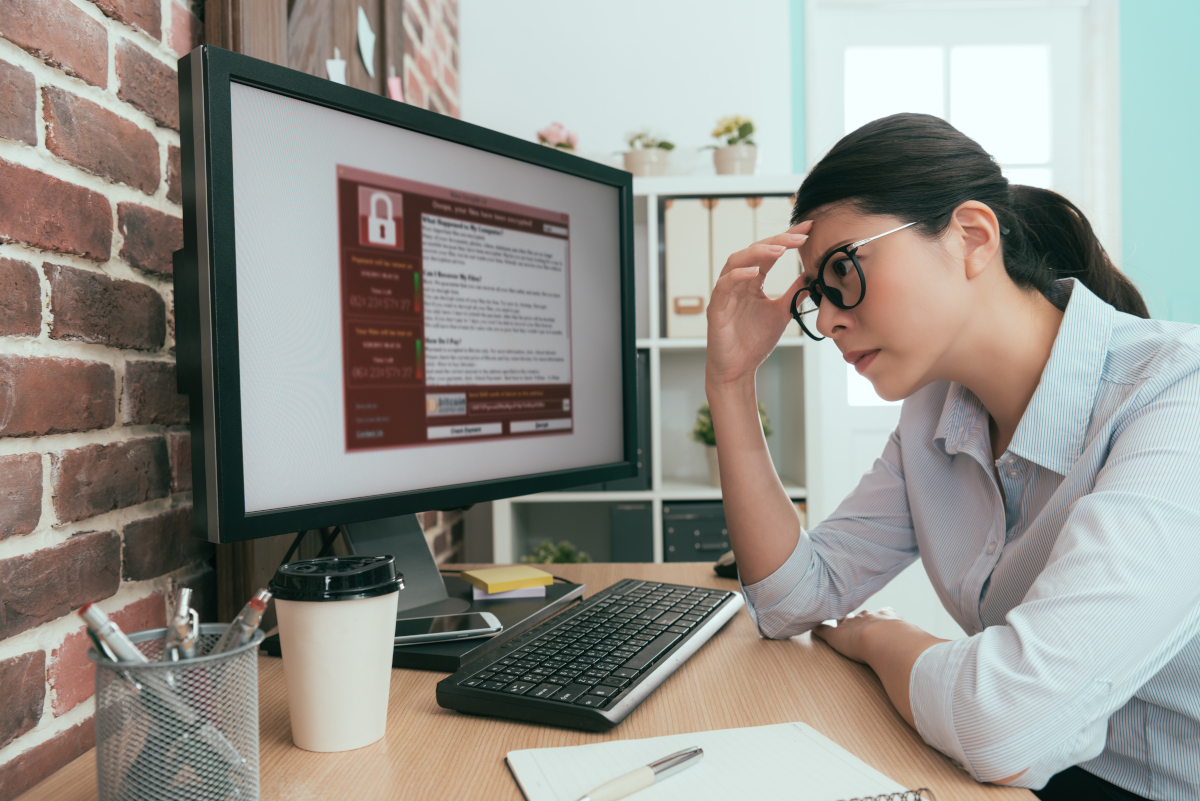 A women looking frustratedly at her computer monitor that is being held hostage by ransomware.