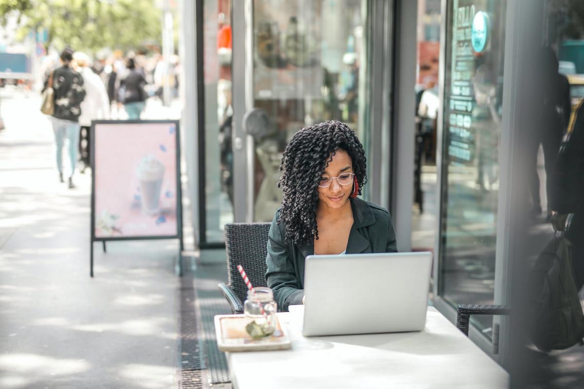 Businesswoman seated outside of coffee shop using laptop computer. Cyber security, remote work, networking, secure computing concept.