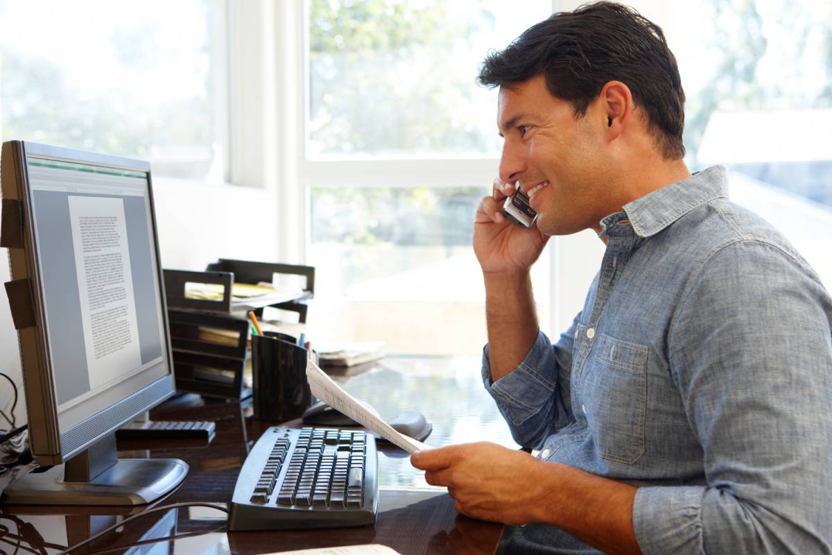 A man working from home using a computer and a phone