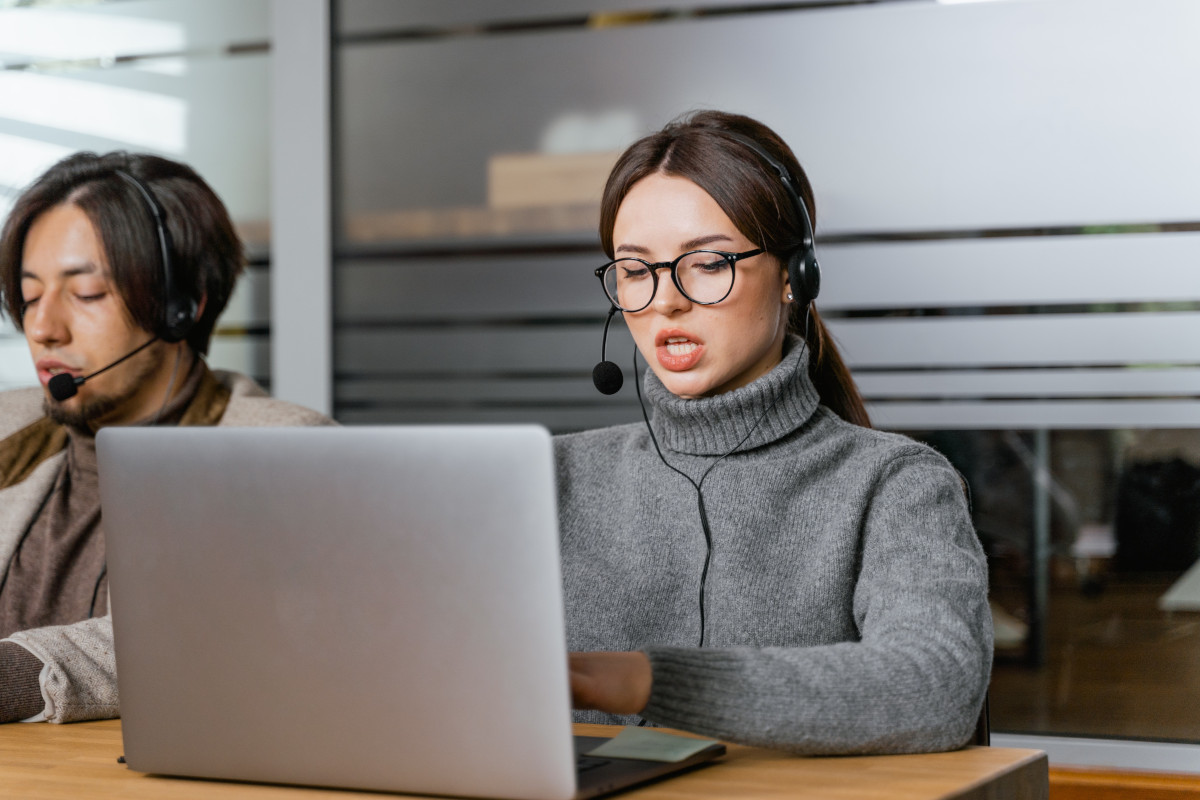 A woman working in a call center using a headset and a laptop and wearing a gray turtleneck