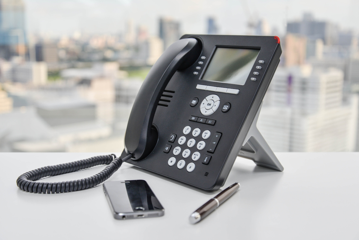 A modern office phone on a desk, with a cellphone and pen next to it