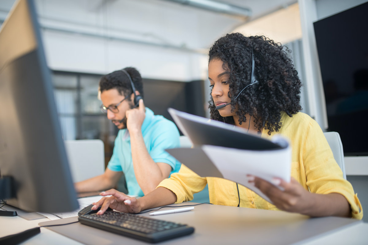 Woman wearing yellow shirt in a call center, using VoIP headset on desktop computer