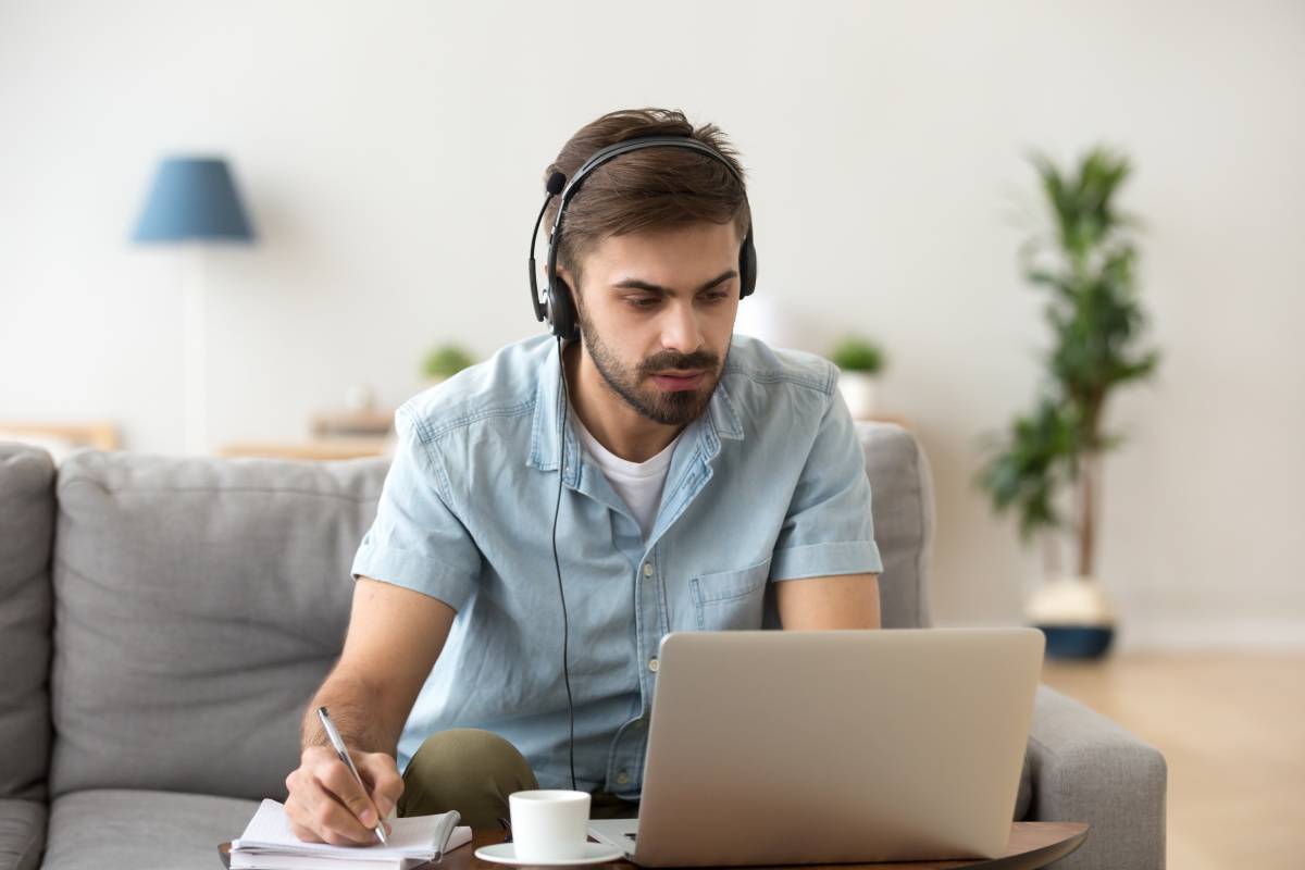 A man working from home using a headset and a laptop, writing on a piece of paper