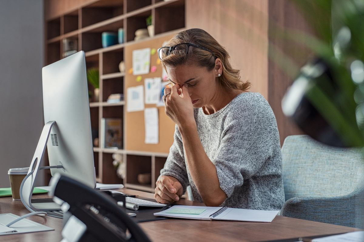 A Women sitting at her desk, pinching the bridge of her nose in frustration