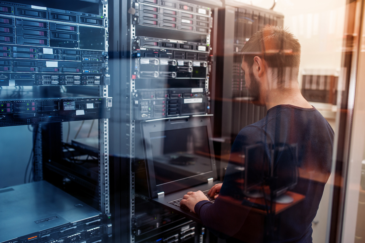 Young engineer with laptop in a network server room.