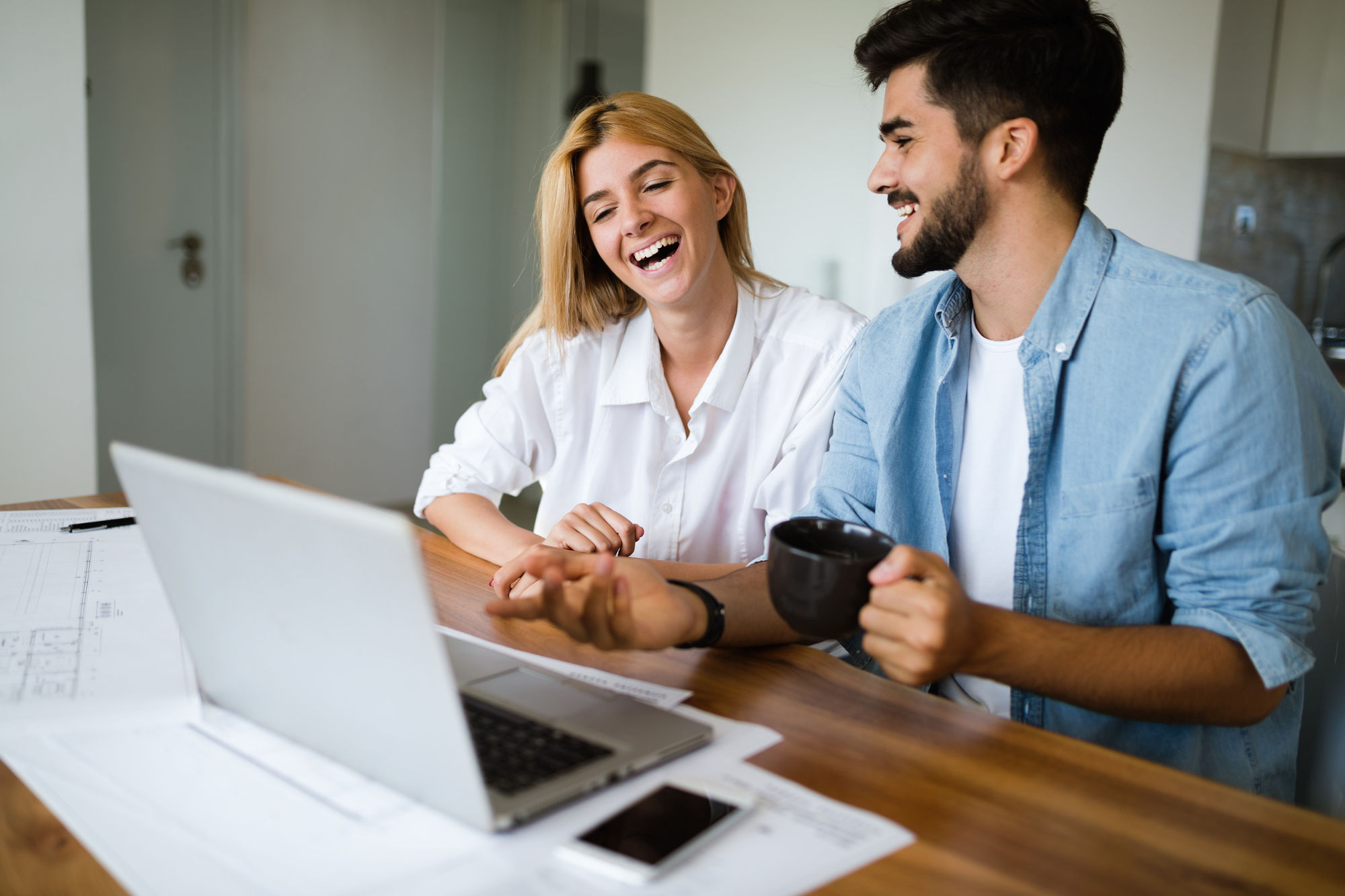 Young man and woman laughing while sitting at a desk with a laptop